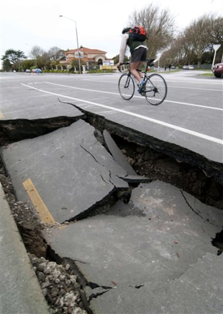 A person cycles past a damaged road near the Avon River following Saturday's powerful 7.1-magnitude earthquake, in Christchurch, New Zealand, Sunday, Sept. 5.